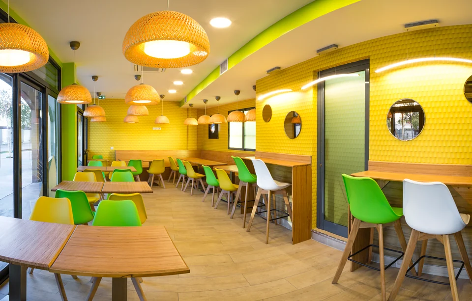 La salle de Noo Wok Colombes, ses tables en bois, ses chaises vertes et ses suspensions tressées